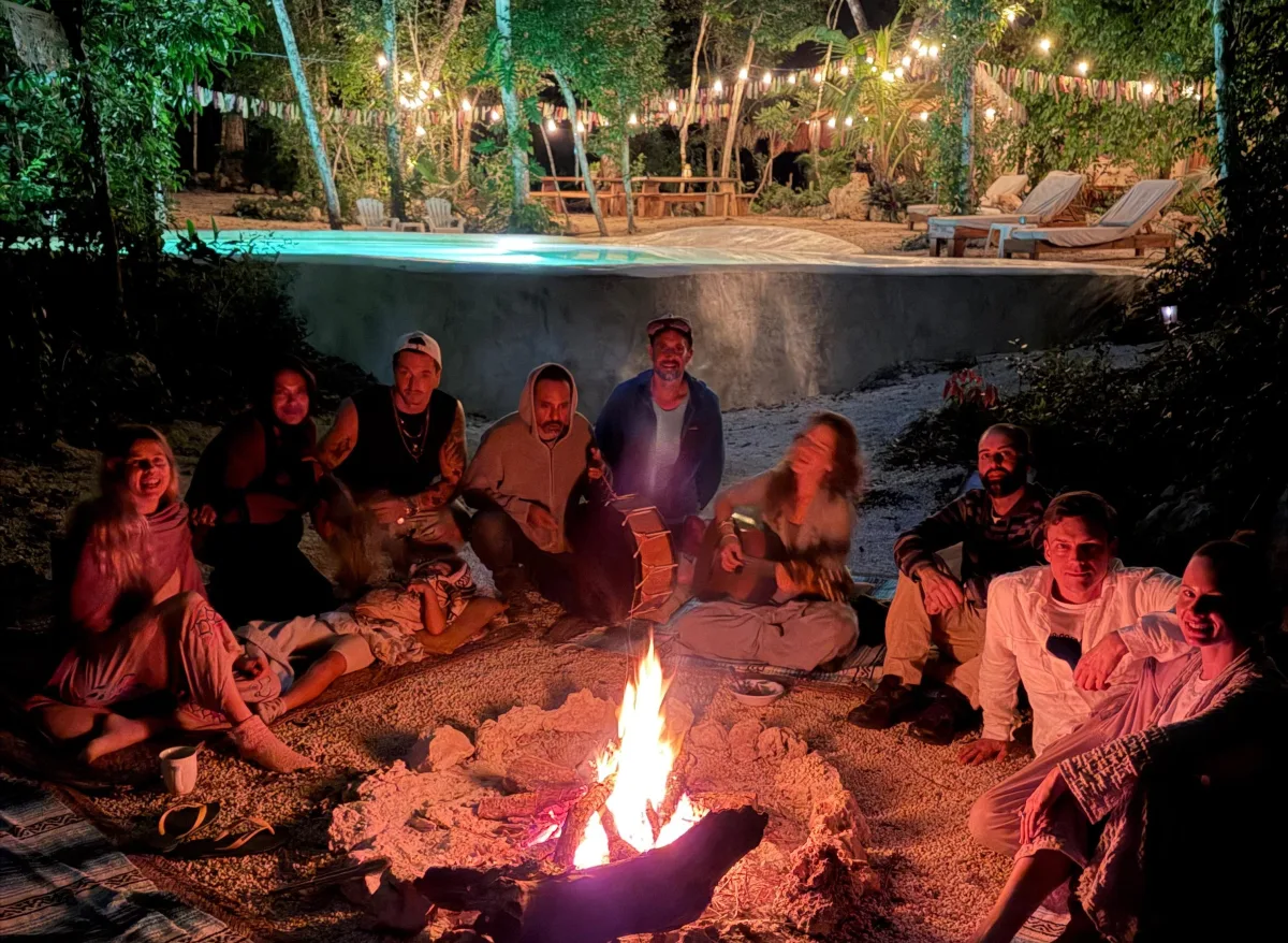 Friends and family gathered around the sacred bonfire — the cenote-fed pool glowing behind